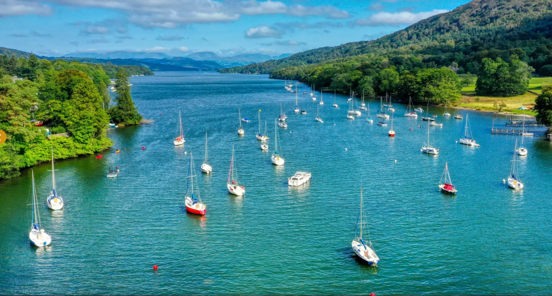 Sailing boats on Lake Windermere surrounded by wooded fells